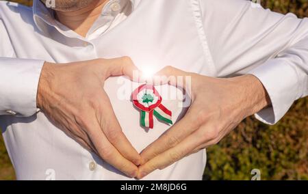 Ein Mann plädiert auf ein weißes Hemd mit dreifarbigen Rosetten Symbol des ungarischen Nationalfeiertags 15. märz die Hände hüpfen in Herzform um die Rosette herum Stockfoto