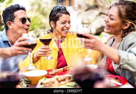 Fröhliche Freunde mit echter Stimmung beim Trinken von Rotwein auf der PIC nic Party - gemischte Altersgruppen, die Spaß zusammen auf der Terrasse des Restaurant Weinguts vor dem Hotel haben Stockfoto