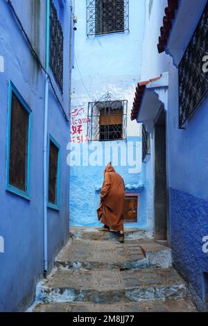 Nordafrika. Marokko. Chefchaouen. Ein alter Mann, gekleidet in einem Bournous, der in einer blauen Straße der Medina spaziert Stockfoto