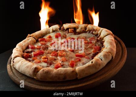 Neapalitanische Pizza mit Tomaten auf dunklem Hintergrund mit Feuer. Pizza in Flammen kochen. Pizza mit Flammen im Hintergrund Stockfoto