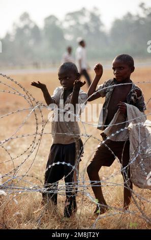 Zairianische Kinder schauen durch das Konzertina-Kabel um den Flughafen, wo Hilfsgüter für die ruandischen Flüchtlinge geliefert werden. Betreff Operation/Serie: SUPPORT HOPE Base: Goma Country: Zaire (ZAR) Stockfoto