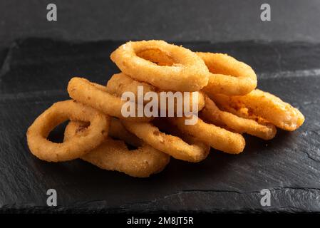 Calamari-Ringe frittiert in Panade. Knusprige Tintenfischringe auf dunklem Hintergrund mit Sauce. Stockfoto