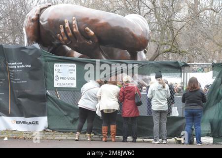 Boston, Massachusetts, USA. 14. Januar 2023. Die Menschen versammeln sich auf dem Boston Common zur Enthüllung der „Umarmung“, einer Skulptur, die Martin Luther King gewidmet ist. Die Königsfamilie war anwesend, ebenso Gouverneur Healy. Einige hoben die Planen an, die an Kettengliederzäunen angebracht waren, um einen Blick vor der Enthüllung zu werfen. Kredit: ZUMA Press, Inc./Alamy Live News Stockfoto