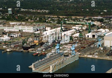 Die Newport News Shipbuilding & Drydock Corporation am James River aus der Vogelperspektive. Auf Trockendock Nr. 11 befindet sich das neue Fahrzeug-Transportschiff BILLILAND (T-AKR-298) des Military Sealift Command. Im Trockendock rechts von AKR-298 befindet sich der nuklearbetriebene geführte Raketenkreuzer USS LONG BEACH (CGN-9), der deaktiviert wird. Basis: Newport News Bundesstaat: Virginia (VA) Land: Vereinigte Staaten von Amerika (USA) Stockfoto