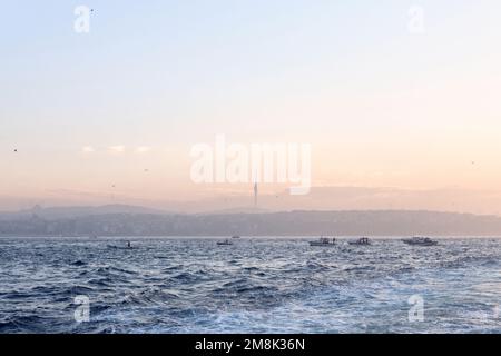 Istanbul, Türkei - Januar 2023: Fischerboote, die auf dem Bosporus Marmarameer angeln, wenn die Sonne hinter der anatolischen Skyline mit dem Camlica Tower aufgeht Stockfoto