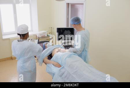 Der Arzt führt zusammen mit dem Assistenten eine Ultraschalluntersuchung des Patienten im OP durch Stockfoto