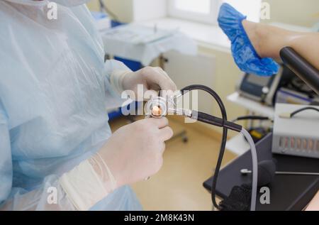 Ein männlicher Arzt in einem weißen Mantel und Gummihandschuhen, der ein Darmskop in einem Keks hält, bereitet sich auf die Operation vor. Stockfoto