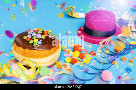 Karnevalsdonut aus Deutschland mit Schokoladenzucker auf blauer Oberfläche mit Konfetti und Luftschlangen - Hintergrund für eine Karnevalsparty oder Party Stockfoto