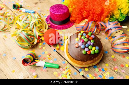 Krapfen-, berliner- oder Karneval-Donut aus Deutschland mit Puderzucker auf einer hellen Holzoberfläche mit Konfetti und Luftschlangen darauf. Stockfoto