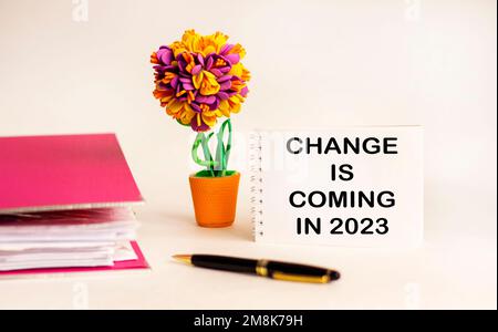 Notizblock mit Textänderungen in 2023 mit einem Stift, einem Ordner für Dokumente und einer Blume auf einem weißen Tisch. Änderungen ab 2023 Stockfoto