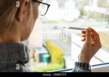 corona COVID-19-Infektion Frau schaut auf das klinische Thermometer in Quarantäne - bleiben Sie zu Hause Stockfoto