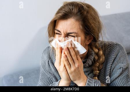 Eine Frau, die im Wohnzimmer in ein Taschentuch niest. Grippe, Medizin und Gesundheitswesen Konzeptbild Stockfoto