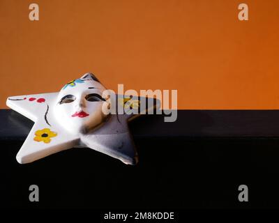 Kleine sternförmige venezianische Maske Hand bemalt auf einem orange-schwarzen Hintergrund - Venedig - Italien Stockfoto