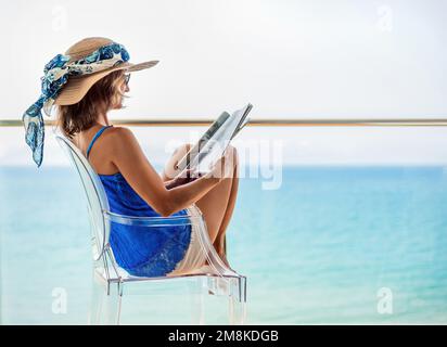 Detailansicht einer Frau mit Hut, die auf einer Hotelterrasse sitzt und eine Zeitschrift liest. Konzepturlaub an der spanischen Küste. Stockfoto