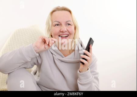 Lächelnde Geschäftsfrau mittleren Alters lächelt über Smartphone sprechen angenehme Gespräche mit dem Kunden, weibliche Vertriebsleiterin macht erfolgreich Gewinn Stockfoto
