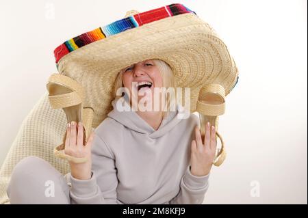 mexikanischer Hut tanzend reife mexikanische Frau mit Sombrero-Hut auf weißem Hintergrund Erwachsene Frau hält wunderschöne hohe Strohschuhe in der Hand, Stockfoto