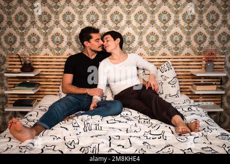 Das junge Paar sitzt auf dem Bett und küsst sich. "Paar-und-Liebe-Konzept". Stockfoto