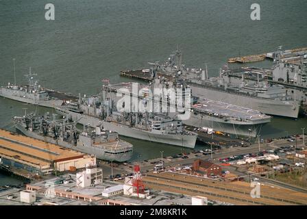 Luftaufnahme der Piers 4, 5 und 6 am Marinestützpunkt Norfolk. Der Nachfüllöler USS Kalamazoo (AOR-6) ist auf der Nordseite von Pier 4 verankert. Das schnelle Kampfhilfsschiff USS Supply (AOE-6) liegt an Pier 5, südlich der Marinefragate USS Estocin (FFG-15) hinter ihr. Das Amphibienschiff USS Saipan (LHA-2) befindet sich auf der Nordseite des Piers. Der stillgelegte Zerstörer Puget Sound (AD-38) ist auf der Südseite von Pier 6 festgebunden und wartet auf den Abtransport an die James River Reserve-Flotte. Das amphibische Angriffsschiff USS Nassau (LHA-4) liegt auf der Nordsi vor Anker Stockfoto