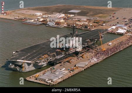 Luftsteuerbord-Viertelansicht des Flugzeugträgers USS America (CVN-66), der nach der Rückkehr von ihrem letzten Einsatz im Mittelmeerraum am Pier 12 festgebunden war. Es ist traditionell so, dass die ersten Männer das Schiff verließen, um während des sechsmonatigen Einsatzes der Schiffe Väter zu werden, damit sie ihre Kinder zum ersten Mal treffen können. Man kann sie sehen, wie sie den Gang von Aufzug zwei hinunterkommen. Basis: Marine Air Station, Norfolk Bundesstaat: Virginia (VA) Land: Vereinigte Staaten von Amerika (USA) Stockfoto