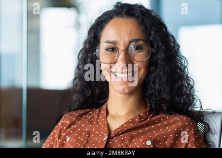 Nahaufnahmen einer wunderschönen lateinamerikanischen Geschäftsfrau, die lächelt und in die Kamera schaut und in einem modernen Büro arbeitet. Stockfoto