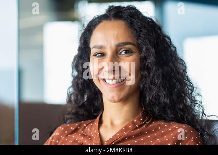 Nahaufnahmen einer wunderschönen lateinamerikanischen Geschäftsfrau, die lächelt und in die Kamera schaut und in einem modernen Büro arbeitet. Stockfoto