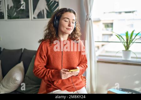 Ruhige junge Frau, die Kopfhörer trägt und zu Hause Musik hört. Stockfoto