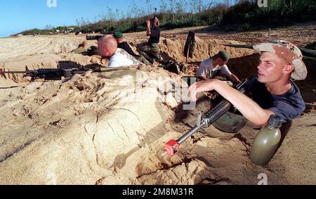 US Marine Corps Lance Corporal Jami Bradshaw (ganz rechts) erwartet ungeduldig die Ankunft einer amphibischen Angriffstruppe, bestehend aus Marines von 11. Marine Expeditionary Unit, Camp Pendleton, Kalifornien, Während er und seine Marinekollegen während der RIMPAC 96, die in der Pacific Missle Range Facility in Barking Sands, Kauai, Hawaii stattfindet, als gegnerische Kraft einen County der Dritten Welt verteidigen. Bradshaw und seine Kameraden sind vom 3. Bataillon, 3. Marines, India Company, in Kaneohe Bay Marine Corps Station, Oahu, Hawaii. Die Marines simulierten mit Platzhaltern ein echtes Kampfszenario Stockfoto