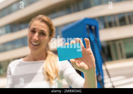 Frau hält NFC- oder RFID-Karte auf einem Hypercharger oder Supercharger für Elektro- oder Hybridfahrzeuge, mit Kopierraum für Ihren individuellen Text. Charg Stockfoto