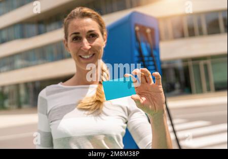 Glückliche Frau, die eine NFC- oder RFID-Karte auf einem Hypercharger oder Supercharger für Elektroautos hält, mit Kopierraum für Ihren individuellen Text. Laden el Stockfoto