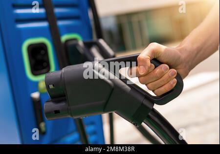 Frau mit einem DC-CCS-Ladeanschluss des Typs 2 an der EV-Ladestation, Frau, die einen Ladeanschluss für Elektrofahrzeuge für das Aufladen vorbereitet Stockfoto