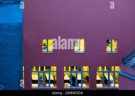 Bürogebäude in der Nacht, Mann sitzt am Schreibtisch in einem beleuchteten Fenster, niedriger Blickwinkel. Leerer Bereich. Beleuchtetes Fenster. Stockfoto