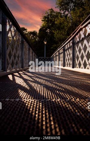 Niedriger Winkel einer Fußgängerbrücke aus Stahl mit Gittergeländern, bei Sonnenschein am späten Abend Stockfoto