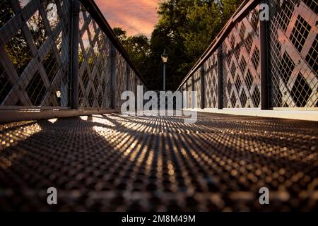 Niedriger Winkel einer Fußgängerbrücke aus Stahl mit Gittergeländern, bei Sonnenschein am späten Abend Stockfoto