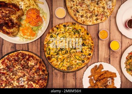 Bild von oben mit frisch zubereiteten Pizzen im Steinofen und verschiedenen Hühnergerichten Stockfoto