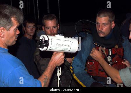 US Navy Hull Technician 1. Class Patrick Wheeler (rechts) hört sich die Anweisungen in letzter Minute auf dem „Pinger Locator“ an, bevor er mit seinem nächsten Tauchgang beginnt. Wheeler ist dem U-Boot-Tender USS EMORY S. LAND (AS 39) zugeteilt und taucht im Rahmen einer Verstärkungskraft, um 24-stündiges Tauchen zu erleichtern, vom Navys-Bergungsschiff USS GREIF (ARS 51). US Navy Boatswains Mate CHIEF Donald Dennis, stationiert an Bord der Greifstation, zeigt den Datasonics „Pinger Locator“, der zur Lokalisierung ferngesteuerter Fahrzeuge (ROVs) verwendet wird. Die Rolle der ROVs bei der Suche nach Leichen vom Absturz des TWA-Fluges 800 war eine Stockfoto