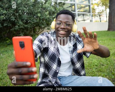 Ein junger afroamerikanischer Mann, der in einem Park mit einem Smartphone telefoniert Stockfoto