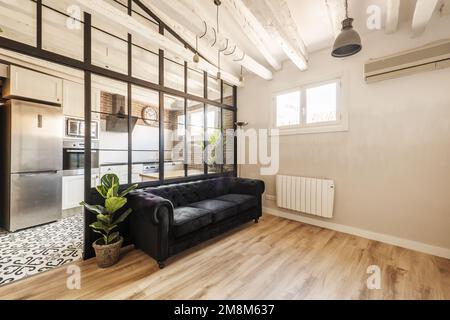 Ferienwohnung im Loft-Stil mit Trennwand aus schwarzem Metall im französischen Stil, schwarzem chesterfield-Sofa mit schwarzem Samt und Decke Stockfoto