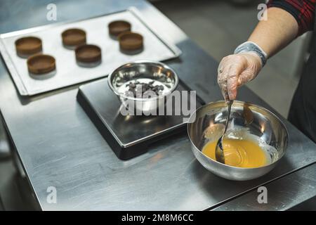 Koch gießt Karamell in eine Schüssel, kreisförmige Formen auf ein Tablett im Hintergrund, Bäckerei. Hochwertiges Foto Stockfoto