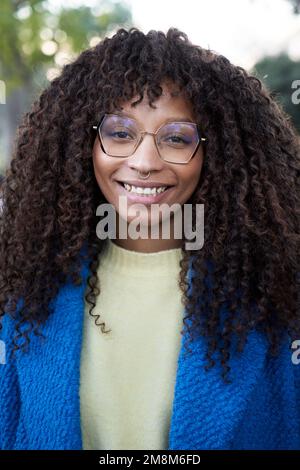 Vertikales Porträt einer lächelnden jungen Afrikanerin mit lockigem Haar und kamerapositivem Ausdruck Stockfoto