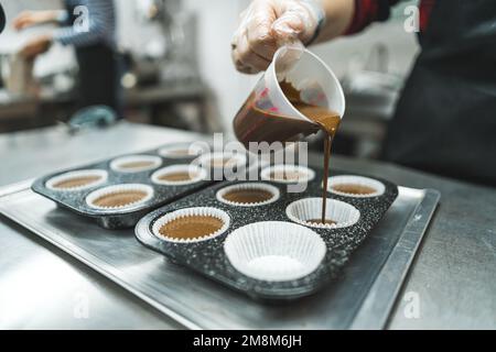 Der Koch gibt den Teig in die Pappbecher, um Schokoladen-Muffins zu backen, Bäckereikonzept. Hochwertiges Foto Stockfoto