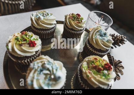 Schokoladen-Cupcakes mit Schlagsahne und Streusel, dekoriert für das Weihnachtsessen, bereiten sich auf weihnachten vor. Hochwertiges Foto Stockfoto