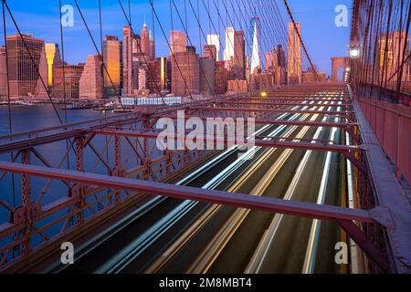 Autoscheinwerfer auf der Brooklyn Bridge bei Sonnenaufgang. Manhattan, New York, USA Stockfoto