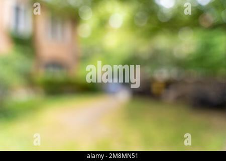 Unscharfer Rasenhintergrund in einem Gartenbereich. Ein leerer Raum in einem Garten kann als Hintergrund in der Konstruktion verwendet werden. Lebhafte Umgebung mit Gebäuden und Bäumen. Stockfoto