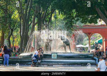 Die Menschen entspannen sich am Fuente de los Coyotes oder Coyote Fountain des mexikanischen Bildhauers Gabriel Ponzanelli im Jardin Centenario im Coyoacan-Viertel von Mexiko-Stadt, Mexiko. Stockfoto