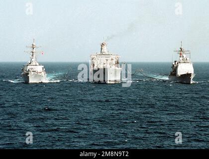 Das von der US-Marine betriebene Ölschiff USNS YUKON (T-AO 202) (Center) führt mit dem geführten Raketenzerstörer USS MILLIUS (DDG 69) (links) und dem geführten Raketenkreuzer USS COWPENS (CG 63) eine doppelte Nachfüllung durch. Alle drei Schiffe werden derzeit zur Unterstützung des Abfangeinsatzes im Seeverkehr in den Persischen Golf eingesetzt. (Unterdurchschnittliches Bild). Betreff Operation/Serie: SÜDLICHES WACHLAND: Persischer Golf Stockfoto