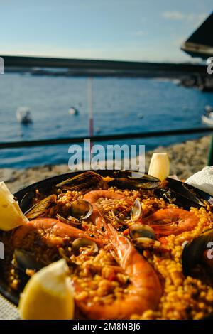 Paella mit einem riesigen Eisenteller, Garnelen und Muscheln, Zitrone. Zum Hintergrund des Meeres in Spanien im Sommer. Stockfoto