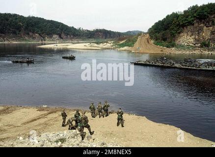 Eine teilweise fertiggestellte Pontonbrücke, die von den 50. Ingenieuren, 1. Zug, Camp LaGuardia, Republik Korea (ROK), errichtet wurde; Fähren zwei m2 Bradley Kampffahrzeuge, die der 2-9. Infanterie, Camp Casey, (ROK), während einer Brückenbauübung und simulierten Überquerung des Imjin River, ROK, am 22. Oktober 1998 zugewiesen wurden. Wenn die Brücke fertiggestellt wäre, würde sie dort beginnen, wo die Soldaten im Vordergrund stehen, und enden direkt am Fuß des Hügels direkt gegenüber dem Fluss von ihnen. Viele der Teilnehmer an der heutigen Übung sind Offiziere, die gemäß dem US Army Officer Professional deve teilnehmen Stockfoto