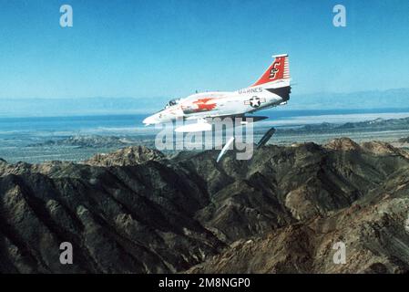 Eine Luft-zu-Luft-Ansicht von links auf ein Marine A-4M Skyhawk-Flugzeug, das zwei Napalmkanister über einem Berggebiet abwirft. Die A-4M ist von Marine Attack Training Squadron 102 (VMAT-102). Eine Luft-zu-Luft-Ansicht von links auf ein Marine A-4M Skyhawk-Flugzeug, das zwei Napalmkanister über einem Berggebiet abwirft. Die A-4M ist von Marine Attack Training Squadron 102 (VMAT-102). Stockfoto