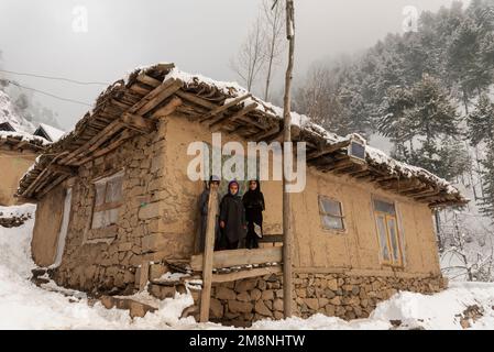 Srinagar, Indien. 15. Januar 2023. Die Kinder stehen vor ihrem Schlammhaus und sehen sich an, wenn sie nach einem schweren Schneefall in den Außenbezirken von Srinagar für ein Foto posieren. Aufgrund des starken Schneefalls gab es mehrere Lawinen an verschiedenen Orten Kaschmirs. Der Zeitraum von 40 Tagen von Dezember 21 bis Januar 31., auch bekannt als Chilai Kalan, in Kaschmir gilt als der wichtigste Zeitraum, wenn es schneit, wird der Zustand noch schlimmer. Kredit: SOPA Images Limited/Alamy Live News Stockfoto