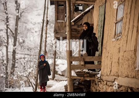 Srinagar, Indien. 15. Januar 2023. Kinder sahen sich vor ihrem Schlammhaus posieren, nachdem es in den Außenbezirken von Srinagar einen schweren Schneefall gab. Aufgrund des starken Schneefalls gab es mehrere Lawinen an verschiedenen Orten Kaschmirs. Der Zeitraum von 40 Tagen von Dezember 21 bis Januar 31., auch bekannt als Chilai Kalan, in Kaschmir gilt als der wichtigste Zeitraum, wenn es schneit, wird der Zustand noch schlimmer. Kredit: SOPA Images Limited/Alamy Live News Stockfoto